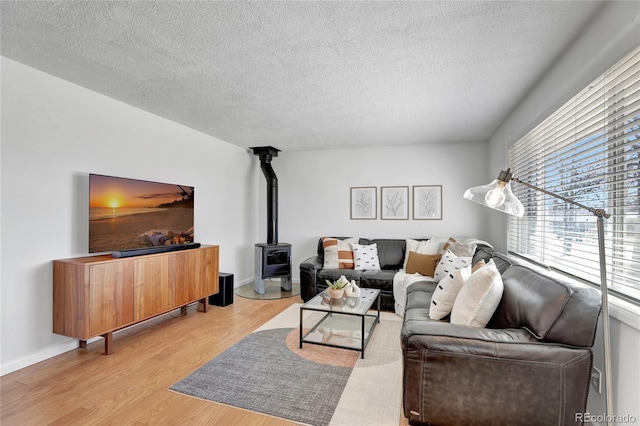 living area with a wood stove, baseboards, a textured ceiling, and light wood finished floors