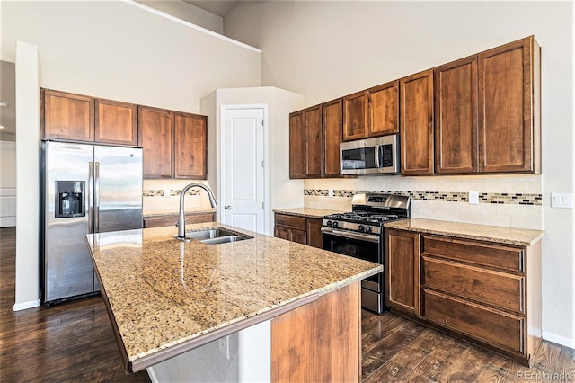 kitchen featuring sink, light stone counters, appliances with stainless steel finishes, a kitchen island with sink, and backsplash