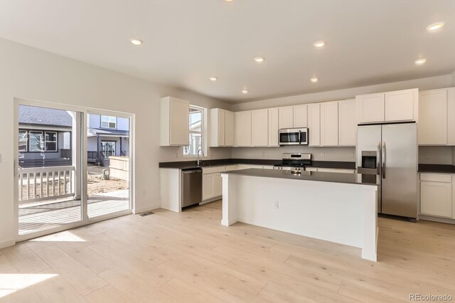 kitchen with dark countertops, light wood finished floors, appliances with stainless steel finishes, and a kitchen island