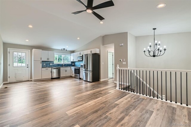 6040 W 75th Dr, Arvada, CO 80003 - kitchen with stainless steel appliances, a chandelier, light wood-style flooring, vaulted ceiling, and white cabinetry