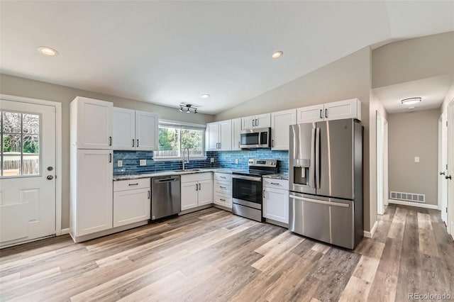 6040 W 75th Dr, Arvada, CO 80003 - kitchen with appliances with stainless steel finishes, decorative backsplash, light wood-style floors, vaulted ceiling, and recessed lighting