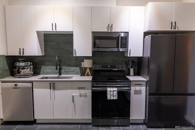 kitchen with a sink, white cabinetry, backsplash, light countertops, and appliances with stainless steel finishes