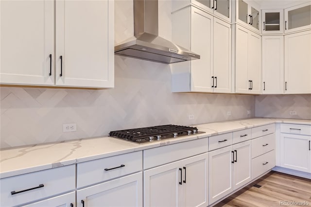 kitchen featuring white cabinetry, wall chimney exhaust hood, light stone counters, stainless steel gas stovetop, and decorative backsplash