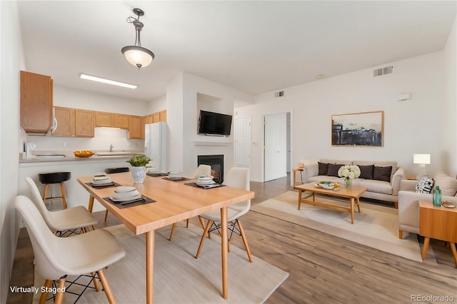 dining space with visible vents, light wood-type flooring, and a glass covered fireplace