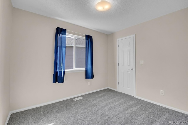 empty room with carpet, a textured ceiling, visible vents, and baseboards