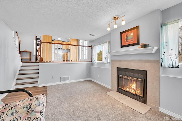 living area with visible vents, stairway, a tiled fireplace, a textured ceiling, and baseboards