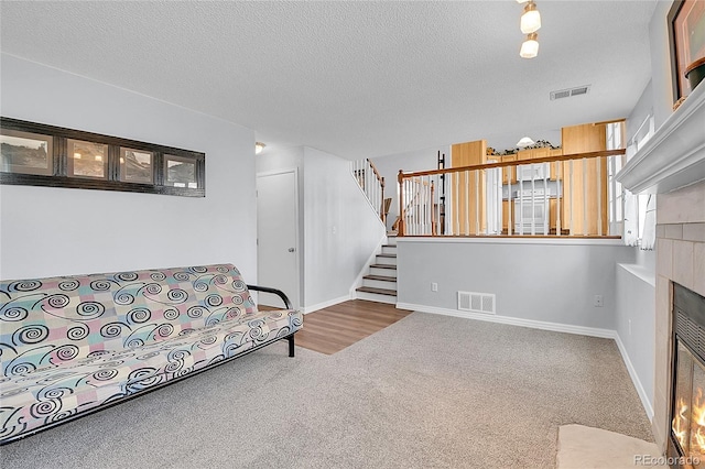 carpeted living area featuring stairs, a fireplace, visible vents, and a textured ceiling