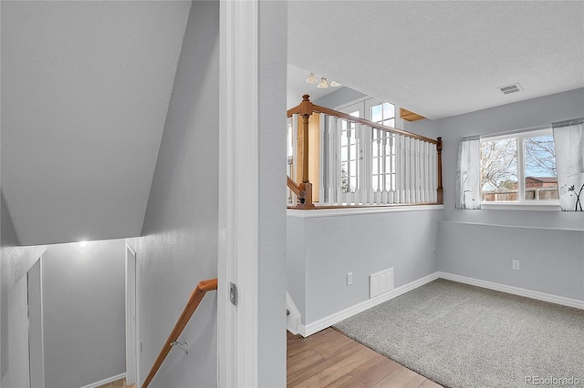 stairs with a textured ceiling, wood finished floors, visible vents, and baseboards