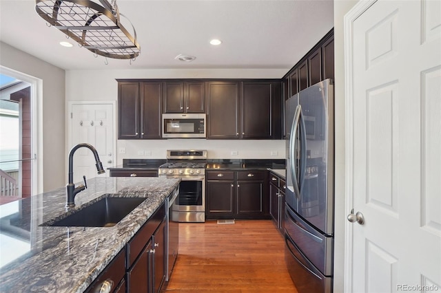 kitchen with hardwood / wood-style floors, sink, dark stone countertops, dark brown cabinets, and stainless steel appliances