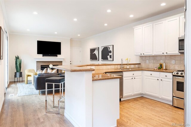 538 Cook St, Denver, CO 80206 - kitchen with stainless steel appliances, light stone countertops, white cabinets, crown molding, and light wood finished floors