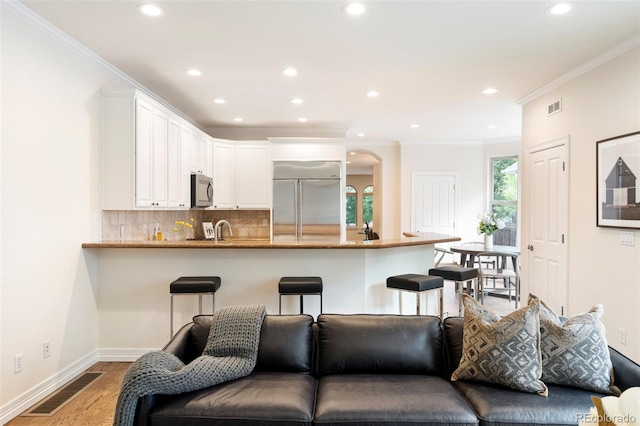 538 Cook St, Denver, CO 80206 - kitchen with appliances with stainless steel finishes, ornamental molding, white cabinetry, backsplash, and light wood-type flooring