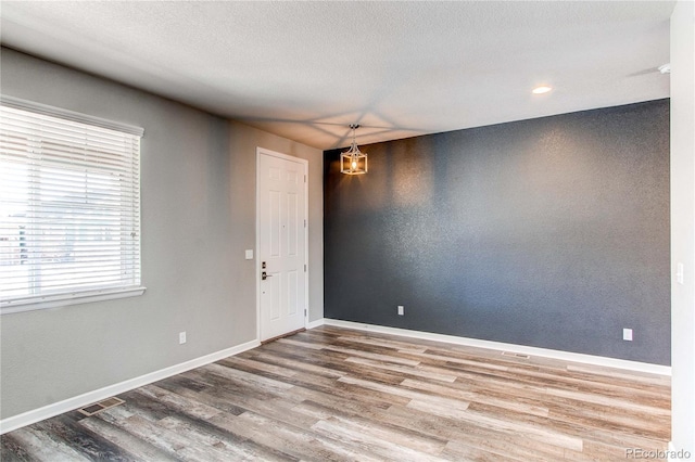 empty room featuring a notable chandelier, hardwood / wood-style flooring, and a textured ceiling