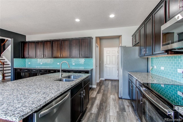 kitchen featuring sink, dark wood-type flooring, appliances with stainless steel finishes, dark brown cabinets, and an island with sink