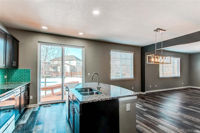 kitchen featuring pendant lighting, sink, an island with sink, and dark wood-type flooring