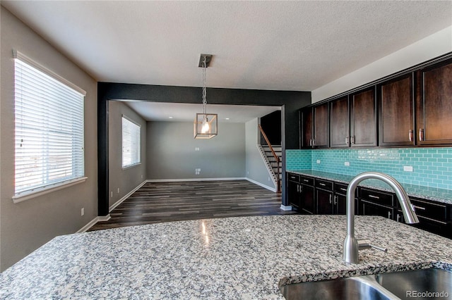 kitchen featuring pendant lighting, sink, dark brown cabinets, light stone counters, and tasteful backsplash