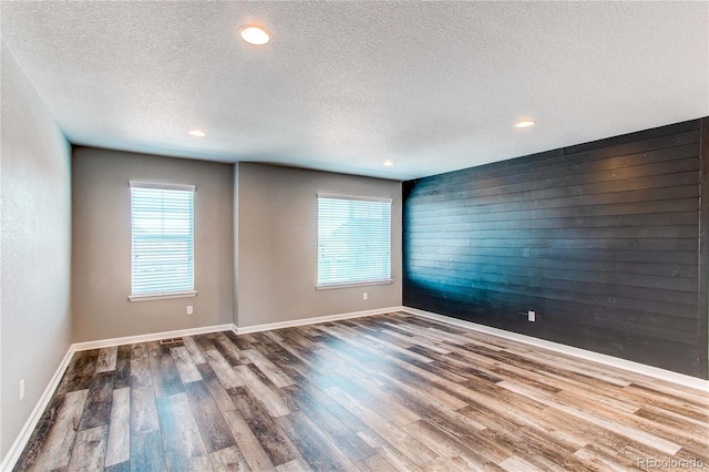 unfurnished room featuring wood-type flooring, wooden walls, and plenty of natural light