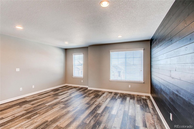 spare room with dark wood-type flooring, a textured ceiling, and wooden walls