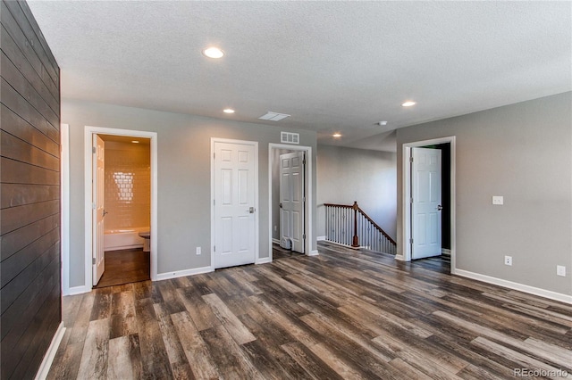 empty room with dark hardwood / wood-style floors, wooden walls, and a textured ceiling