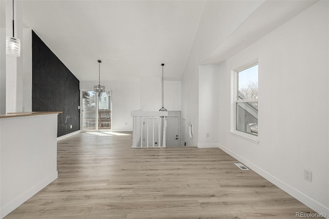 unfurnished living room with visible vents, light wood-style floors, an inviting chandelier, and a healthy amount of sunlight