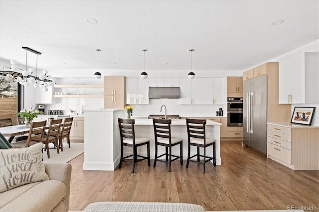 kitchen featuring hanging light fixtures, light hardwood / wood-style flooring, appliances with stainless steel finishes, a kitchen breakfast bar, and a kitchen island with sink