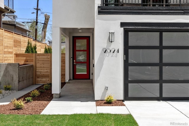 doorway to property featuring stucco siding, a garage, and fence