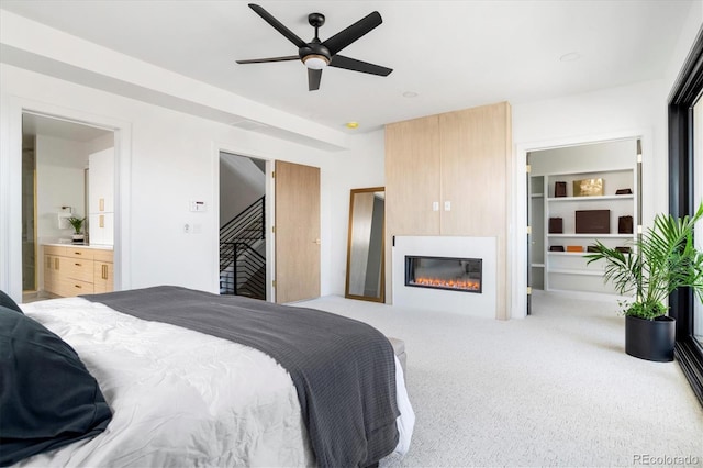 bedroom with carpet floors, a ceiling fan, a large fireplace, and ensuite bath
