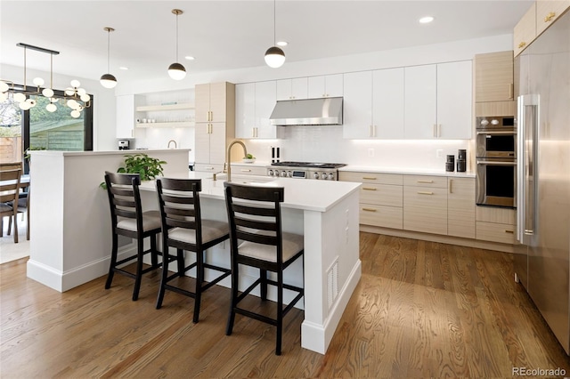 kitchen with light countertops, a breakfast bar area, dark wood-type flooring, under cabinet range hood, and modern cabinets