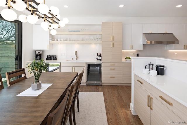 kitchen featuring dark wood-style flooring, wine cooler, under cabinet range hood, a sink, and backsplash