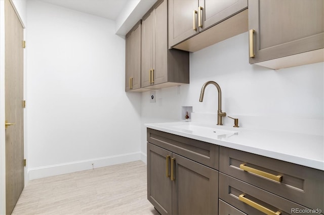 kitchen with a sink, light countertops, baseboards, and light wood finished floors