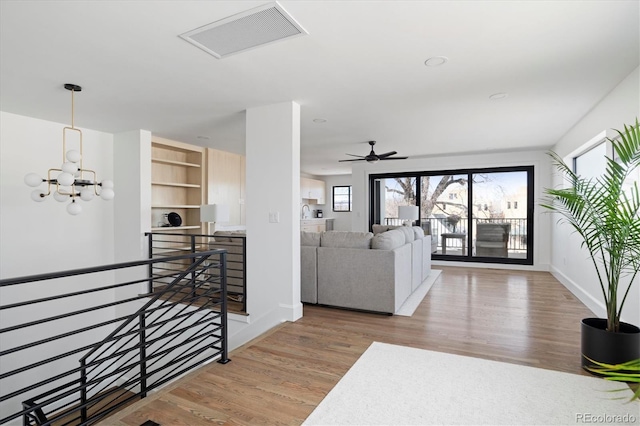 foyer entrance featuring baseboards, visible vents, wood finished floors, and ceiling fan with notable chandelier