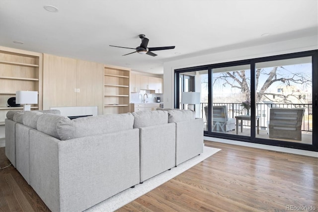 living room with a ceiling fan, built in shelves, and wood finished floors
