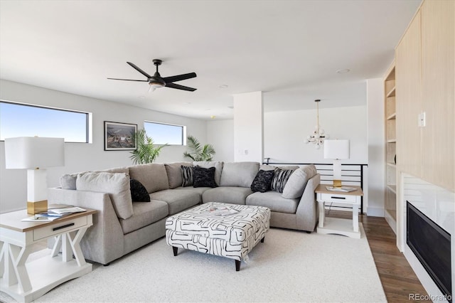 living area featuring built in shelves, a fireplace, ceiling fan with notable chandelier, and wood finished floors