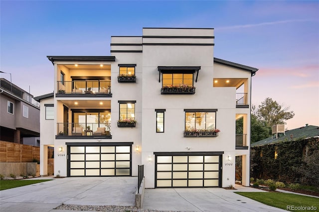 modern home featuring an attached garage, driveway, a balcony, and stucco siding