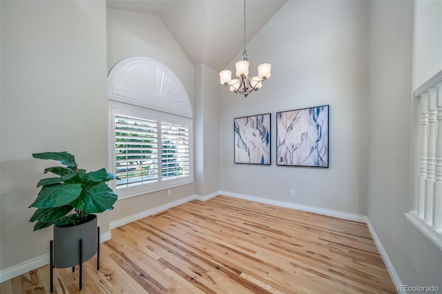 spare room with high vaulted ceiling, hardwood / wood-style floors, and a notable chandelier