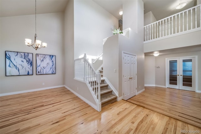 stairway featuring french doors, a towering ceiling, an inviting chandelier, and hardwood / wood-style floors