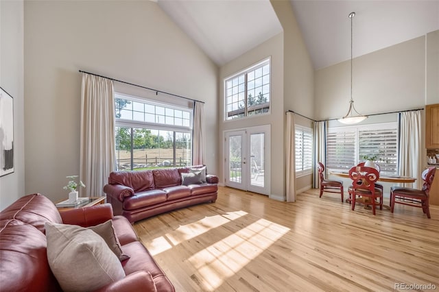 living room featuring high vaulted ceiling, light wood-type flooring, french doors, and a healthy amount of sunlight