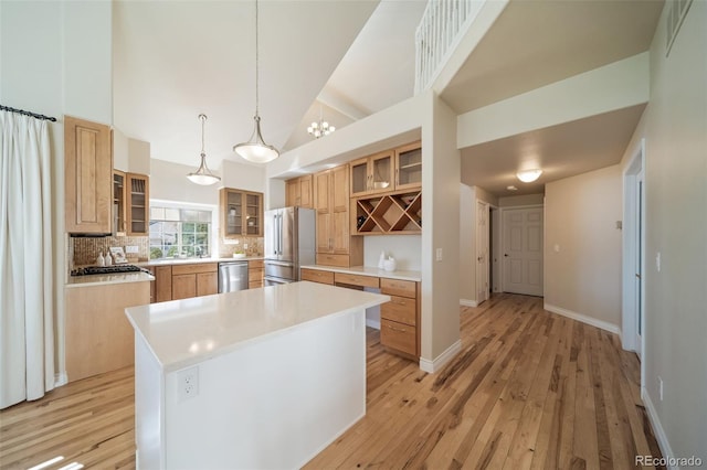 kitchen with appliances with stainless steel finishes, tasteful backsplash, high vaulted ceiling, a kitchen island, and pendant lighting