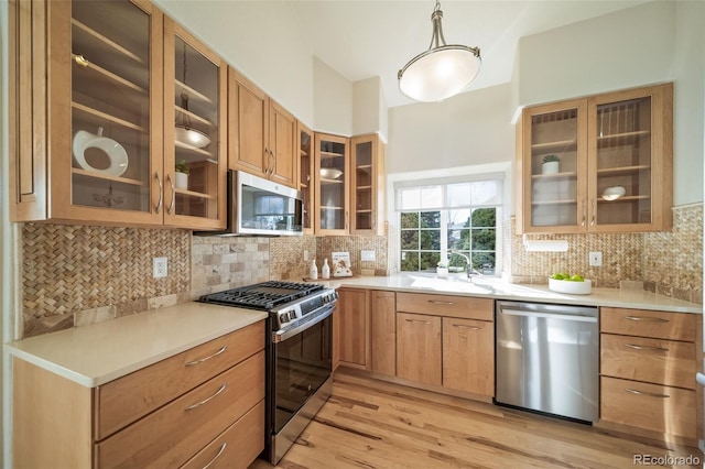 kitchen featuring pendant lighting, stainless steel appliances, decorative backsplash, sink, and light hardwood / wood-style flooring