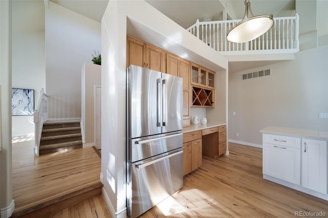 kitchen featuring high vaulted ceiling, white cabinets, light wood-type flooring, and stainless steel refrigerator