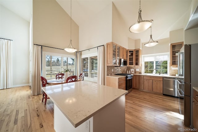 kitchen featuring appliances with stainless steel finishes, light hardwood / wood-style floors, backsplash, hanging light fixtures, and high vaulted ceiling