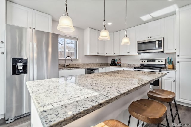 kitchen featuring pendant lighting, white cabinets, a center island, light stone counters, and stainless steel appliances