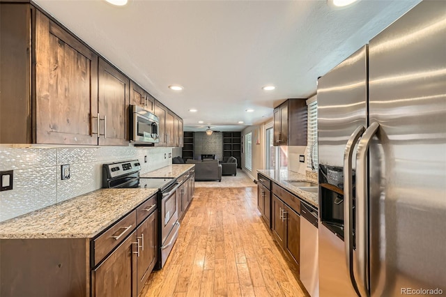 kitchen featuring light wood-type flooring, tasteful backsplash, light stone counters, stainless steel appliances, and ceiling fan