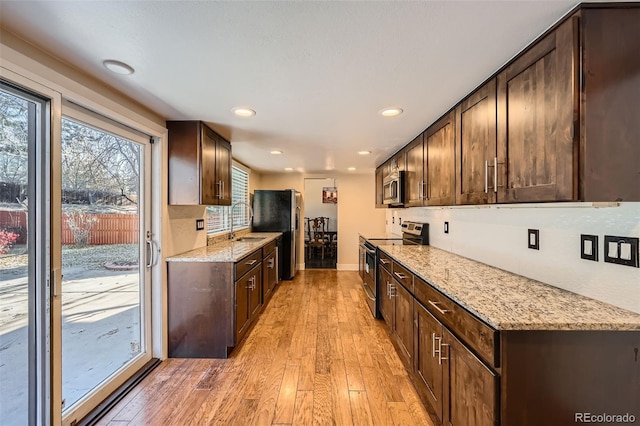 kitchen with sink, appliances with stainless steel finishes, light hardwood / wood-style floors, light stone counters, and dark brown cabinetry