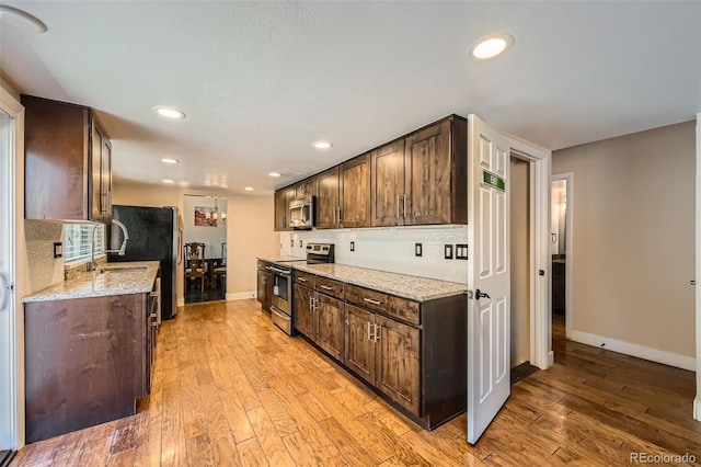 kitchen with dark brown cabinetry, light stone counters, stainless steel appliances, and light hardwood / wood-style floors