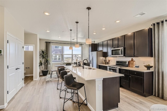 kitchen with pendant lighting, a kitchen island with sink, light hardwood / wood-style flooring, appliances with stainless steel finishes, and a breakfast bar area