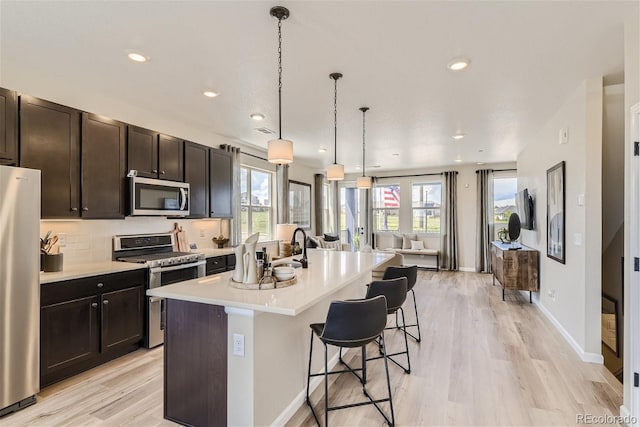 kitchen featuring pendant lighting, a center island with sink, appliances with stainless steel finishes, a kitchen breakfast bar, and light hardwood / wood-style floors