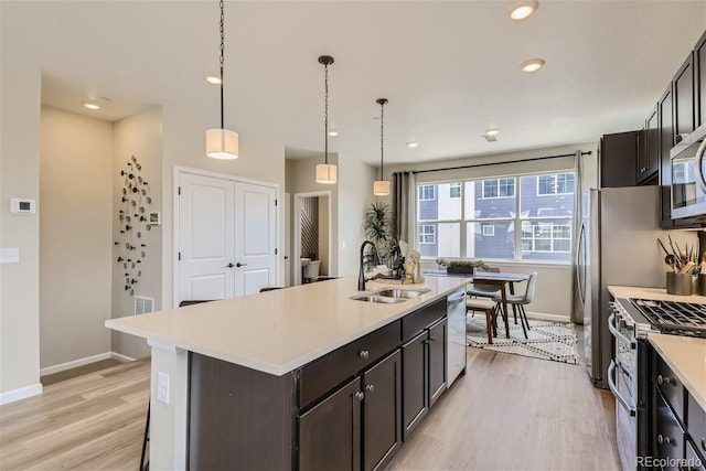 kitchen with an island with sink, hanging light fixtures, sink, light hardwood / wood-style flooring, and stainless steel appliances