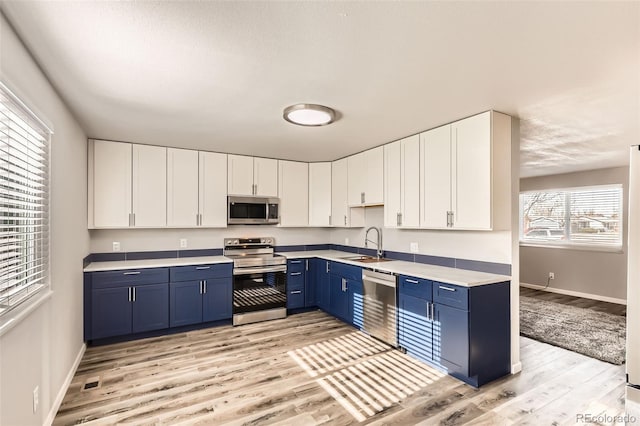 kitchen featuring sink, blue cabinetry, appliances with stainless steel finishes, light hardwood / wood-style floors, and white cabinetry