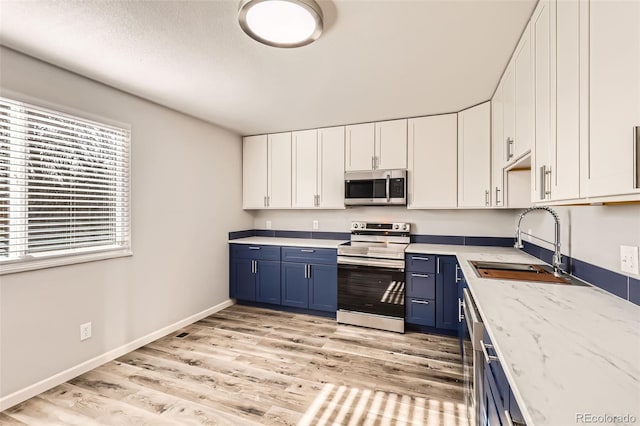 kitchen featuring light wood-type flooring, stainless steel appliances, sink, blue cabinetry, and white cabinets