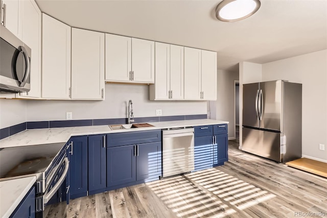 kitchen with light hardwood / wood-style floors, blue cabinets, white cabinetry, and appliances with stainless steel finishes